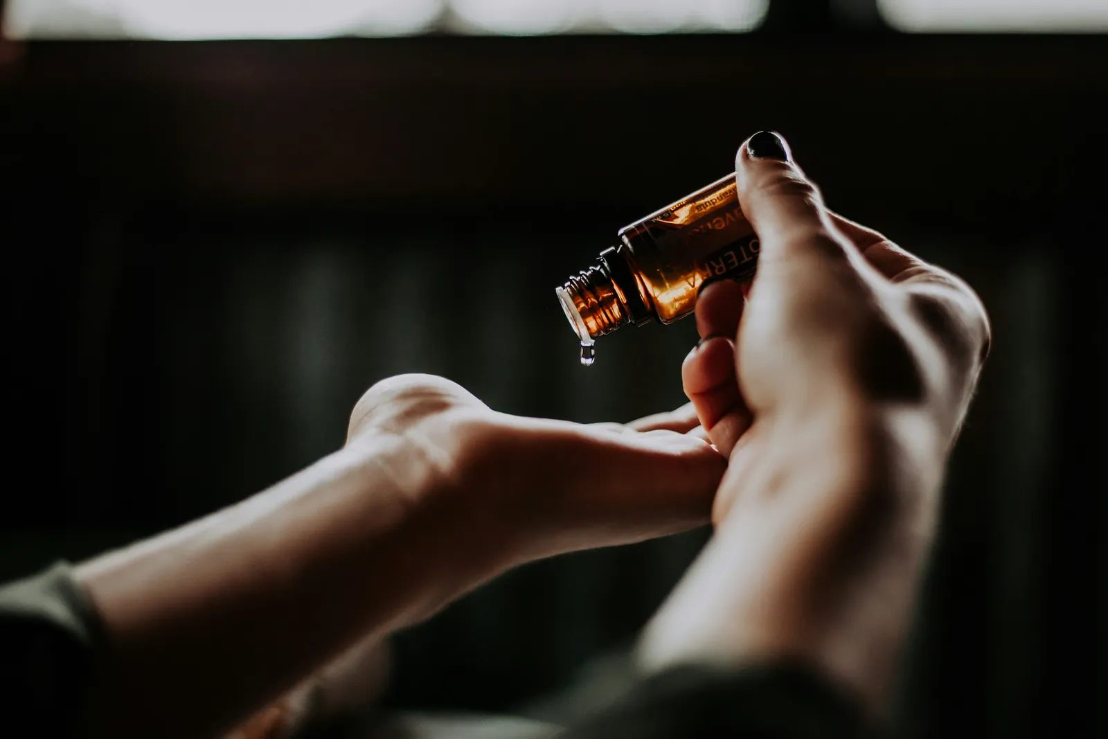 Hands and a small bottle of oil in dim light — a slow moment of caring for yourself